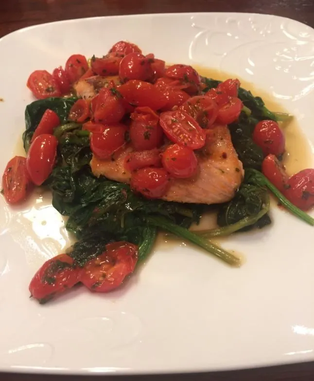 In der Pfanne gebratener Lachs mit sautiertem Spinat und Tomaten